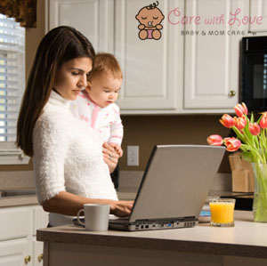 Mother holding baby and typing on laptop computer in kitchen.